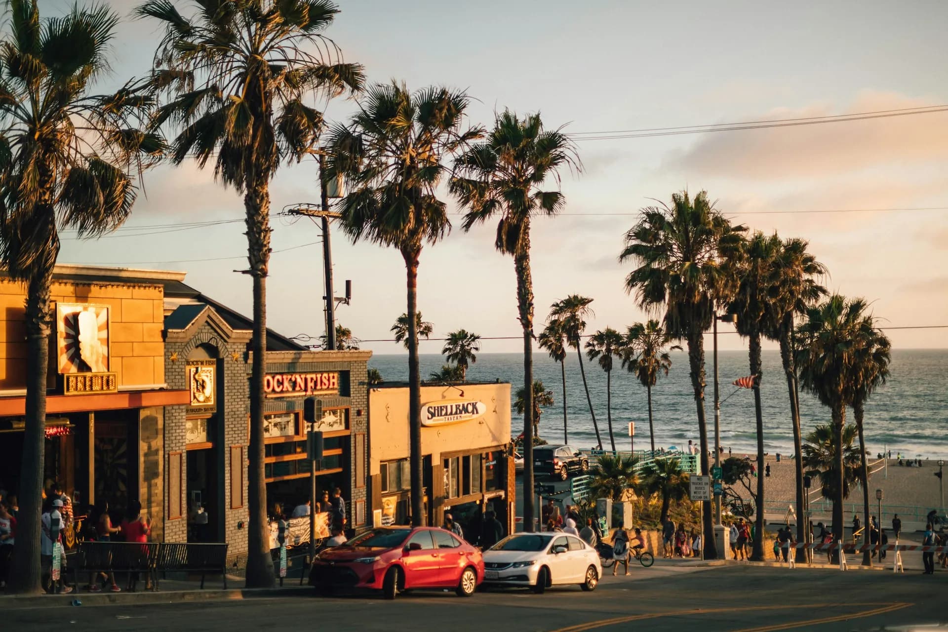 Sunny street view looking down toward the ocean in Manhattan Beach, Los Angeles, lined with palm trees and local restaurants, highlighting the coastal lifestyle available near South Bay Assisted Living communities.