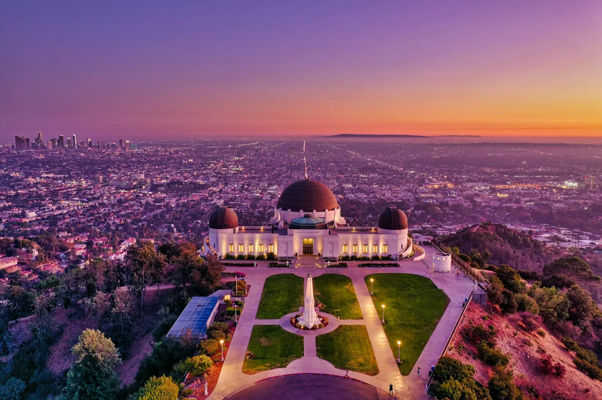 A twilight aerial photograph looking down at the illuminated Griffith Observatory with the vast Los Angeles city lights and downtown skyline in the background, highlighting the central location of local Assisted Living options.